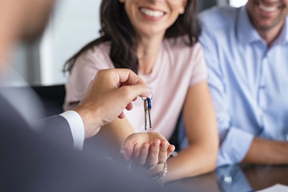 Close up of man hand giving house keys to woman. Smiling mature woman receiving new house keys from real estate agent. Man delivering keys to client for new home. Real estate agent giving keys.
